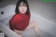 A woman in a red sweater sitting in a bathtub.