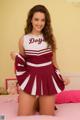 A woman in a cheerleading uniform posing on a bed.