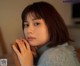 A woman in a blue sweater leaning against a wooden chair.