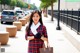 A woman in a red and black plaid dress holding a brown bag.