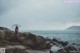 A woman standing on a rocky beach holding an umbrella.