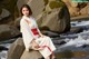 A woman in a white kimono sitting on a rock by a river.